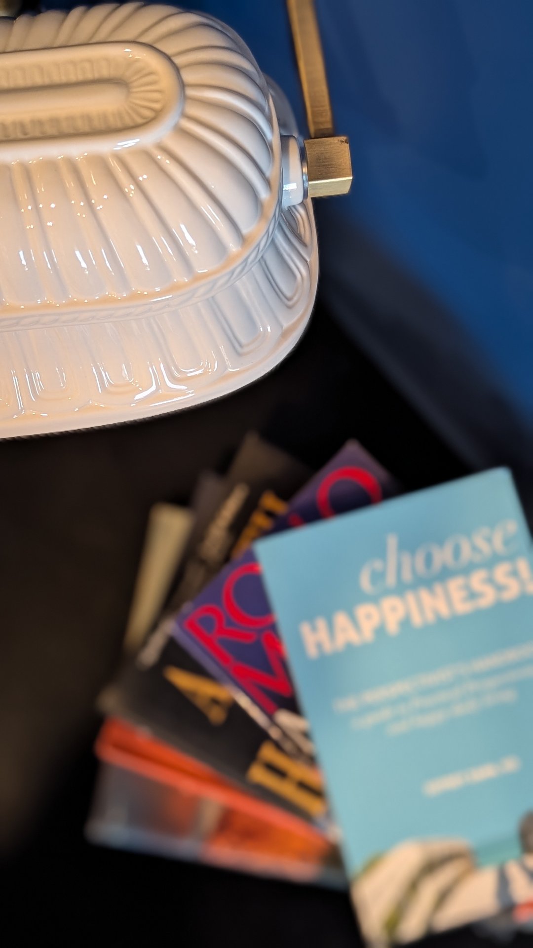 Ceramic ribbed lamp on a stack of books including Choose Happiness, against a deep blue wall